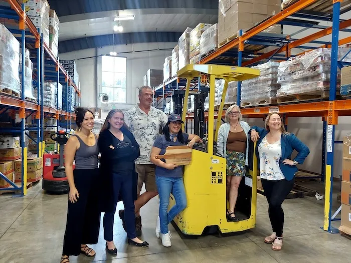 Community Resource team and partners posing beside a forklift in the Josephine County Food Bank warehouse