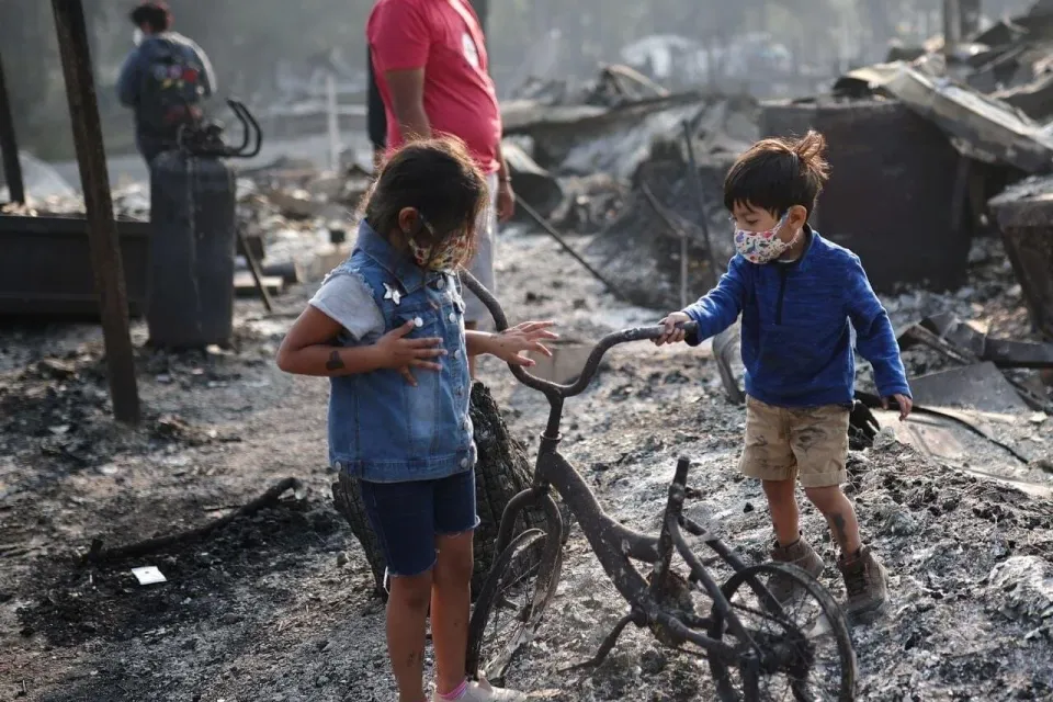 Dos niños junto a una bicicleta dañada por el fuego, entre las cenizas que dejaron los incendios del sur de Oregón