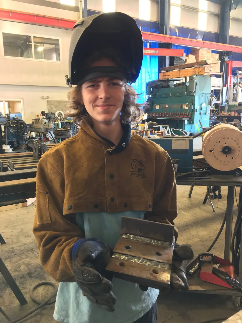 Loegan Weigert con equipo de soldadura sosteniendo una pieza soldada en el taller de Pro-Weld