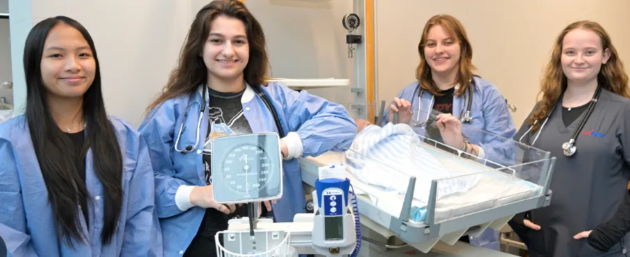 Cuatro estudiantes de Career Build con uniforme médico practicando cuidado de pacientes en un laboratorio de capacitación en salud